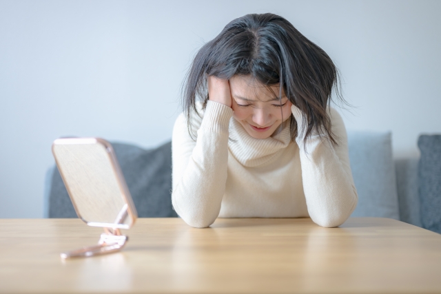 鏡と頭を抱える若い女性