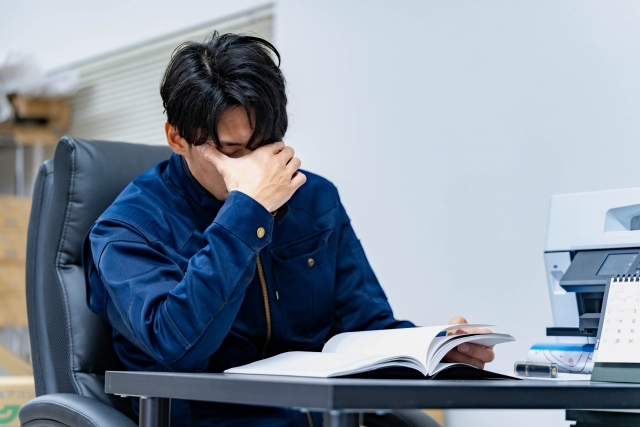 椅子に座って悩む作業服の男性