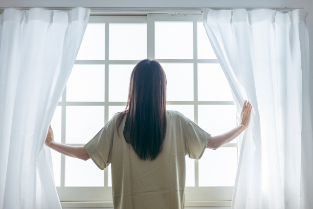 窓を開けるミドル世代の女性（起床）