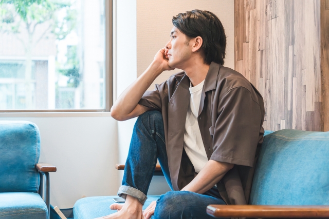 ソファに座って考え事をする男性(悩む)