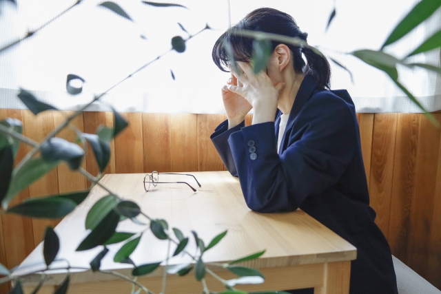 顔を覆って座っているジャケット姿の女性